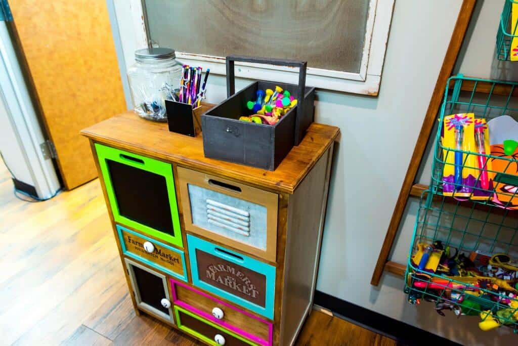 activity center with wood color cabinet with various size ans shape drawers each frames in a different color, some with a white knob and some with a black wide handle